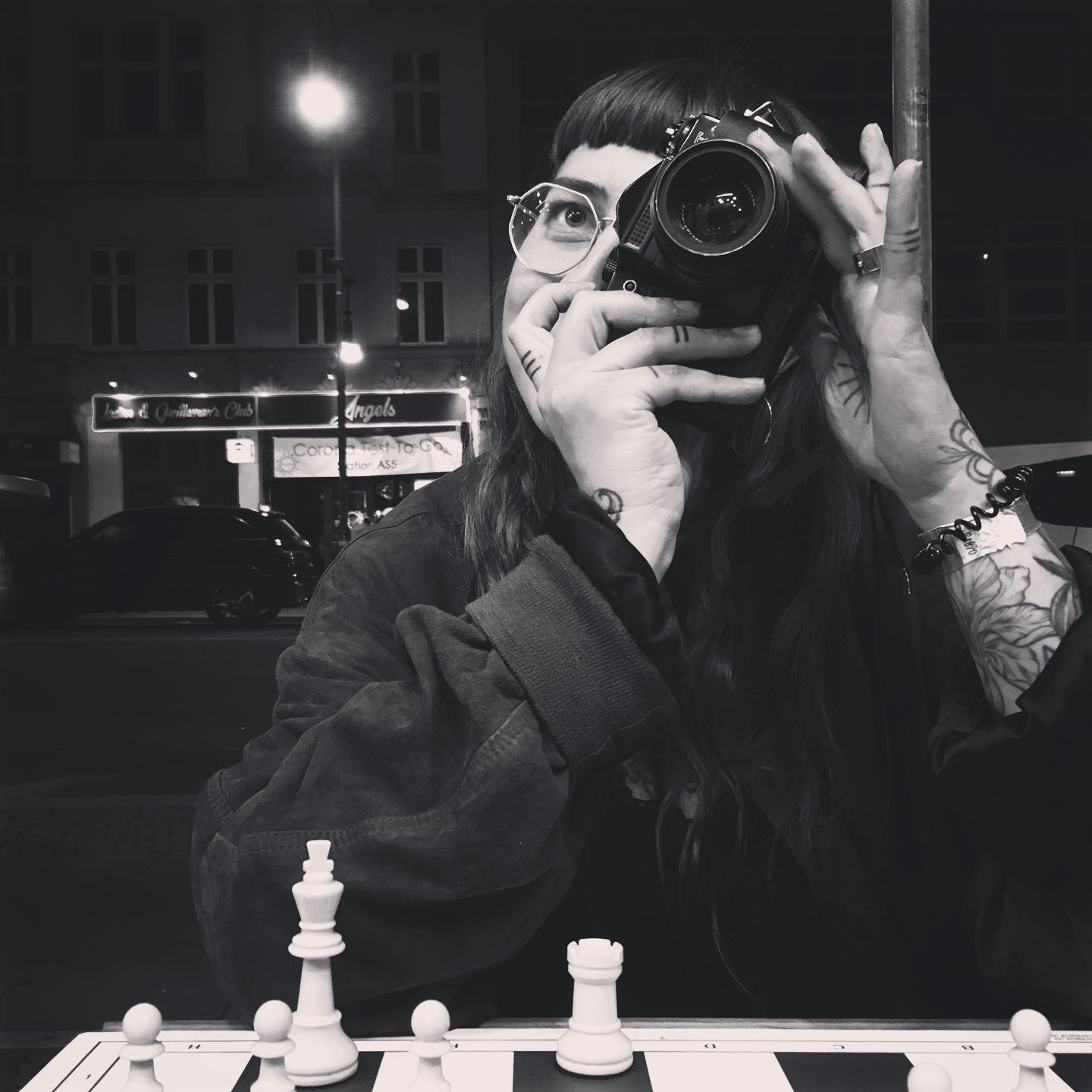 A girl sitting at the chess board holding up her photo camera