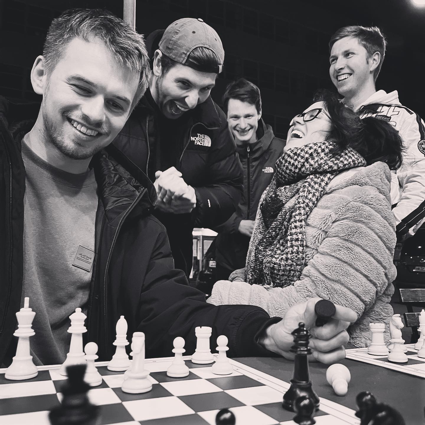 A group of people around a chess board laughing and cheering